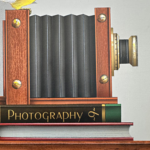 Detail of Photorealistic acrylic painting of a Goldfinch sitting atop an old camera and two books, one titled "Photography 9", against a white background by James Carter - Cottage Curator - Sperryville VA Art Gallery