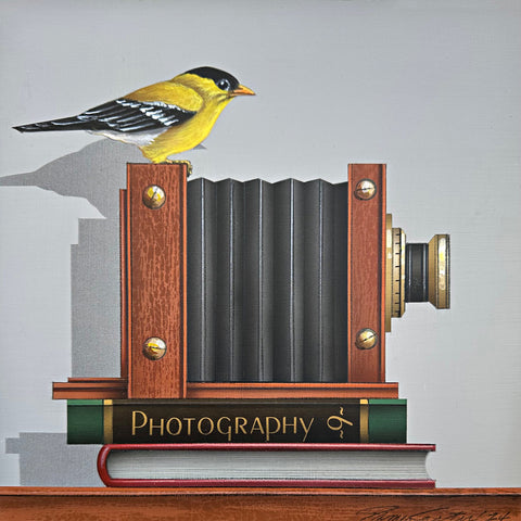 Photorealistic acrylic painting of a Goldfinch sitting atop an old camera and two books, one titled "Photography 9", against a white background by James Carter - Cottage Curator - Sperryville VA Art Gallery