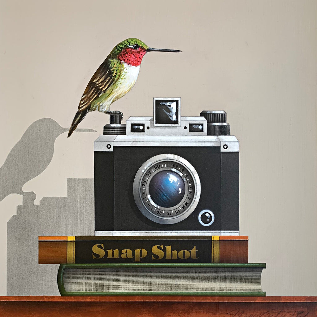 Painting of a ruby-throated hummingbird perched atop a vintage camera on two books, one titled Snapshot, on a tabletop by James Carter at Cottage Curator - Sperryville VA Art Gallery