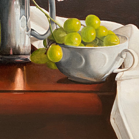 Detail of still life of tabletop with white cloth, pewter mug and green grapes in a white teacup against a reddish-brown background by Liisa Strandman-Long at Cottage Curator - Sperryville VA Art Gallery